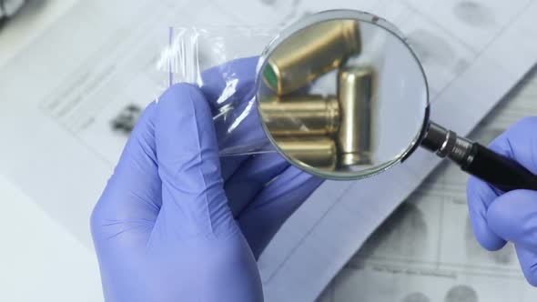 Investigator Analyzing Bullets Evidence From Murder Scene Using Magnifying Glass alt