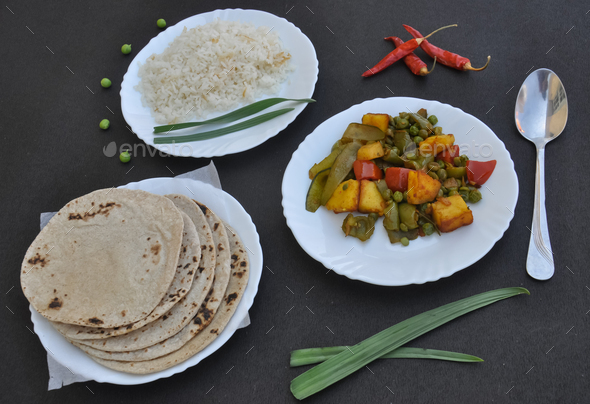 Rice, matar paneer mix veg and roti (Indian bread) on white plate over black background