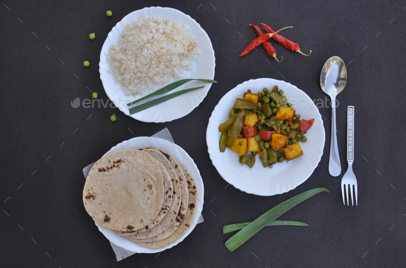 Top view of matar paneer mix veg, rice and chapati (Indian bread) on white plate