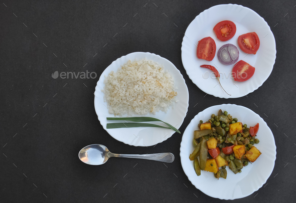 Overhead view of rice, matar paneer mix veg and salad on white plate over black background