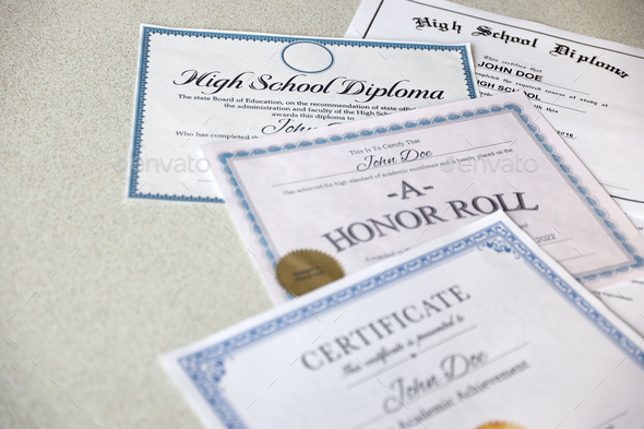 A honor roll recognition, certificate of achievement and high school diploma lies on table