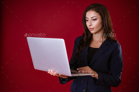 Young woman decides business cases in a laptop on a red studio background.