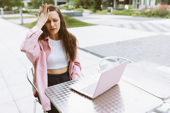 Young woman with laptop with facepalm gesture, feeling regret, sorrow, blaming herself for mistake - Stock Photo - Images