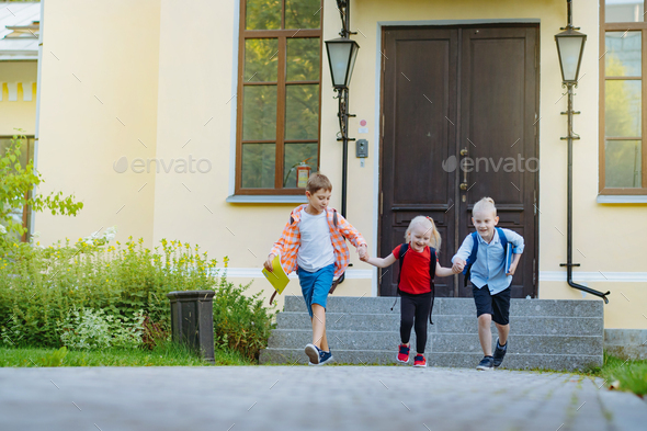 Happy caucasian children running from school with backpacks on sunny day. Begining of academic year - Stock Photo - Images