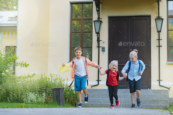 Happy caucasian children running from school with backpacks on sunny day. Boys laughing plaing fool - Stock Photo - Images