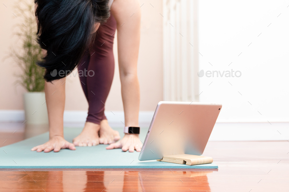 Stylish Asian woman practice yoga asana from online exercise class with computer tablet at home