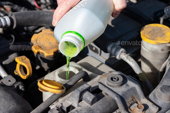 Hand with bottle pouring antifreeze coolant into the expansion tank