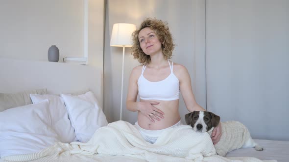 Smiling Pregnant Woman Relaxing In Bed With Her Dog alt