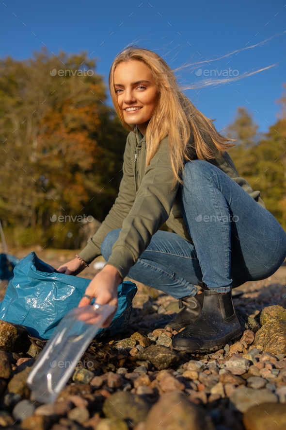 Smiling young woman in environment conservation team picking up plastic at beach - Stock Photo - Images