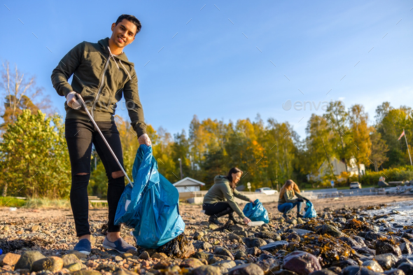 Man cleaning beach with group of volunteers on sunny day - Stock Photo - Images