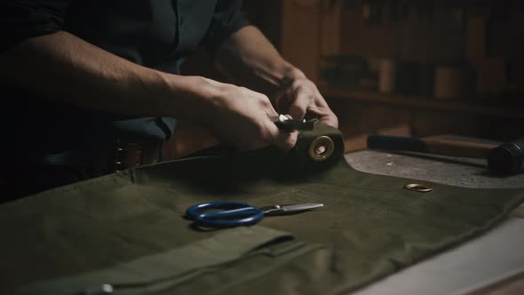 Close Up of Unrecognizable Tailor Unpicking Canvas Fabric at Workshop Working with Knife in Evening alt
