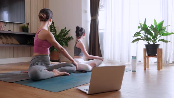 Mother and girl practicing yoga together by watching live video tutorial with laptop at home