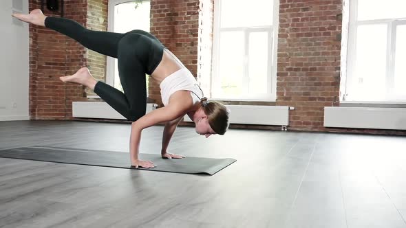 Young Slim Caucasian Woman in Sportswear Standing in Bakasana Pose on Mat at Gym