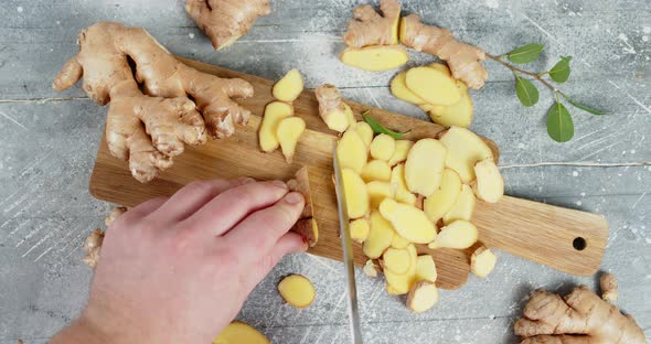 Male Hand with a Knife Slice the Ginger on a Cutting Board.  alt
