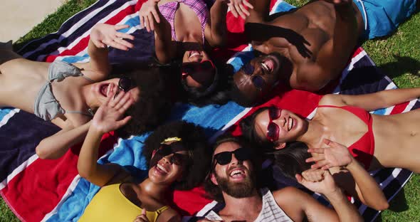 Diverse group of friends sunbathing together smiling and waving to camera alt