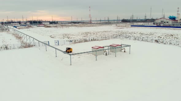 A Drone Flies Over an Industrial Area in a Snowy Area a Miniloader Tractor Clears the Snow From the alt