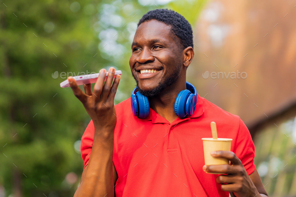 young afro american man with headphones on neck using smartphone in summer park - Stock Photo - Images