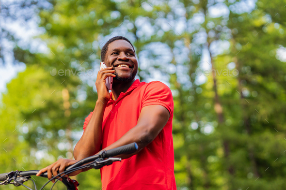 afro american man in red t-shirt walking in park with a bicycle - Stock Photo - Images