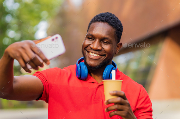 young afro american man with headphones on neck using smartphone in summer park - Stock Photo - Images