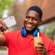 young afro american man with headphones on neck using smartphone in summer park - PhotoDune Item for Sale