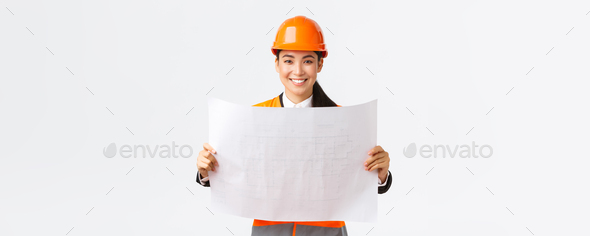 Excited smiling asian female engineer at construction area study blueprints, looking pleased while