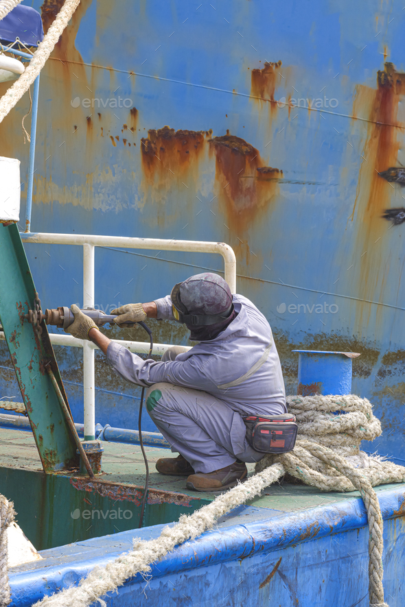 Worker using electric steel cracker to polishing the old rusty stern