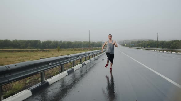 Worried man of athletic build quickly runs along highway in rain, front view. alt