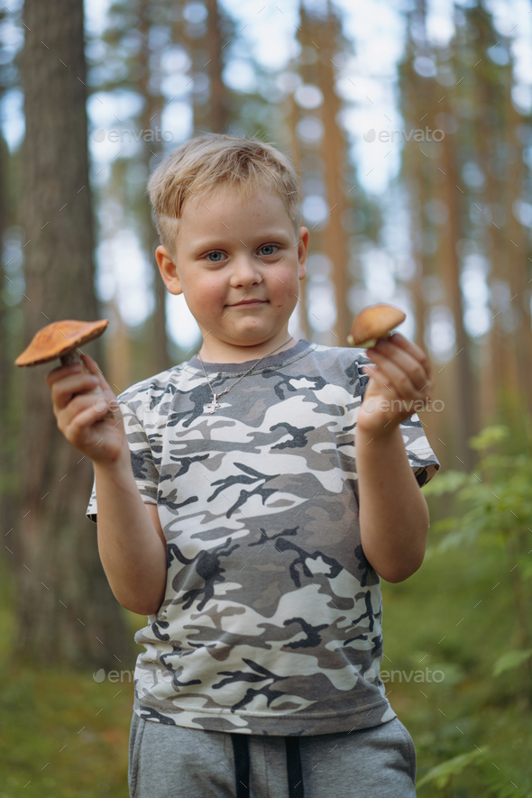 cute blond boy wearing khaki tee shirt and pants in a forest holding found mushrooms in both hands
