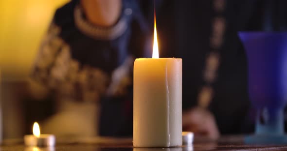 Front View of White Candle Standing on the Table and Female Caucasian Hand Lighting It Up alt