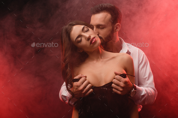 handsome passionate man undressing his girlfriend in red smoky room