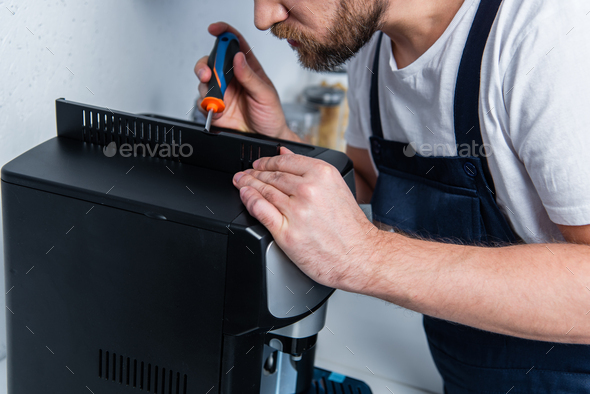 cropped image of handyman in working overall repairing coffee machine by screwdriver in kitchen