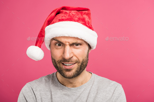 portrait of funny confused man in santa hat, isolated on pink