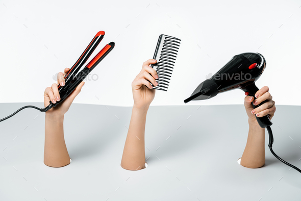 partial view of female hands holding hairstyle tools through holes on white