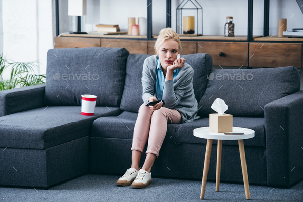 sad woman sittng on couch with bucket of ice cream and tissue box while watching tv in living room