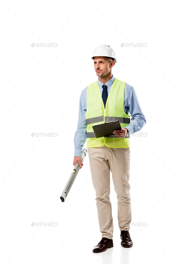 handsome engineer holding spirit level, clipboard and looking away isolated on white