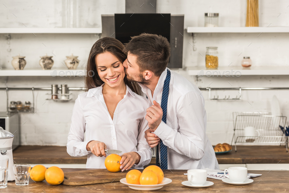 boyfriend kissing girlfriend while she cutting oranges in morning at kitchen, gender stereotypes