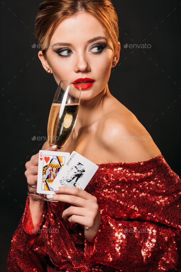 attractive girl in red shiny dress holding joker and queen of hearts cards, drinking champagne