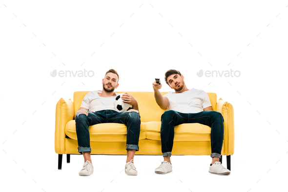 bored men with soccer ball and remote controller sitting on couch and watching tv isolated on white