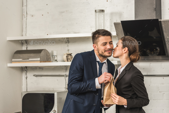 girlfriend giving lunch to boyfriend and kissing him in morning at kitchen, social roles concept