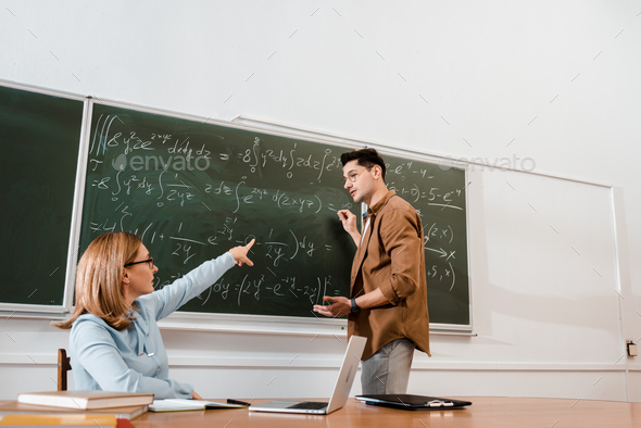 Female professor pointing at chalkboard with equations during lesson