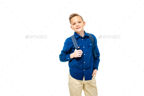 schoolboy in blue shirt with hand in pocket holding backpack straps isolated on white