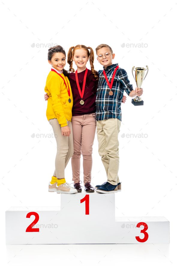 happy kids with medals and trophy cup smiling and standing on winner podium and looking at camera