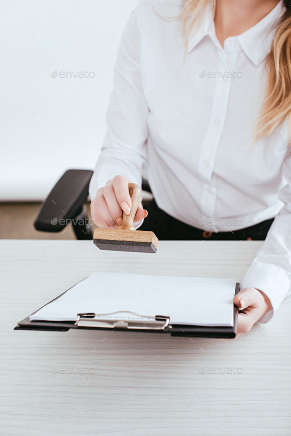 selective focus of female lawyer holding clipboard and stamp in hands