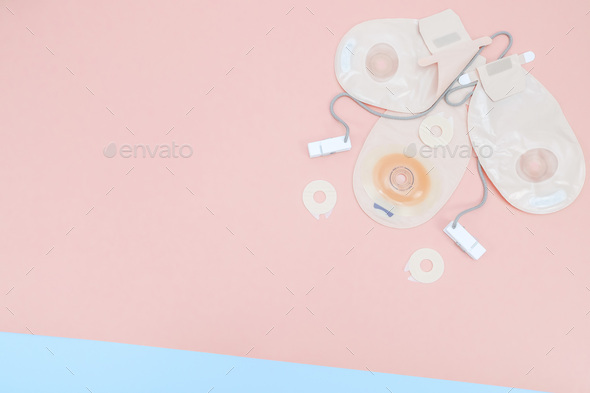 Three colostomy bags with medical clips lie on the right on a blue-pink