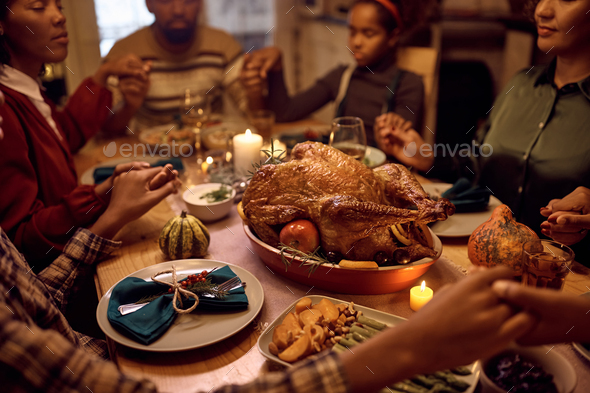 Close up of Thanksgiving turkey with family praying at dining table.