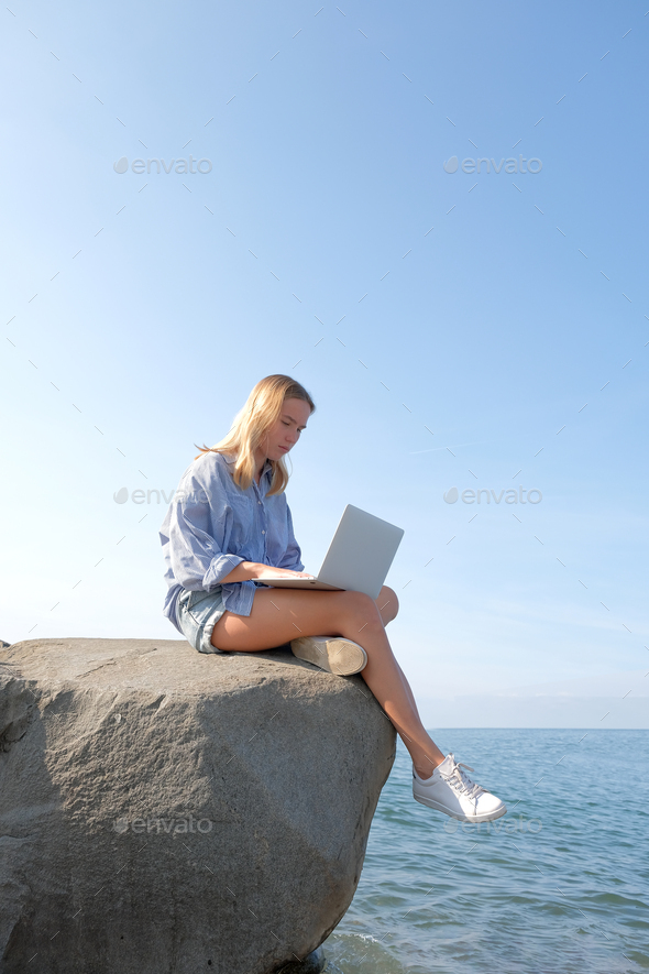 Remote work.Girl freelancer works remotely on the sea shore.workation, remote work,WFVH