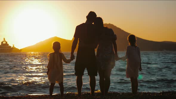 Silhouette of Happy Family Standing on Beach at Sunset and Hugging alt
