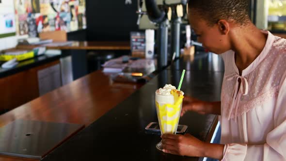 Happy woman talking on mobile phone while having milkshake alt