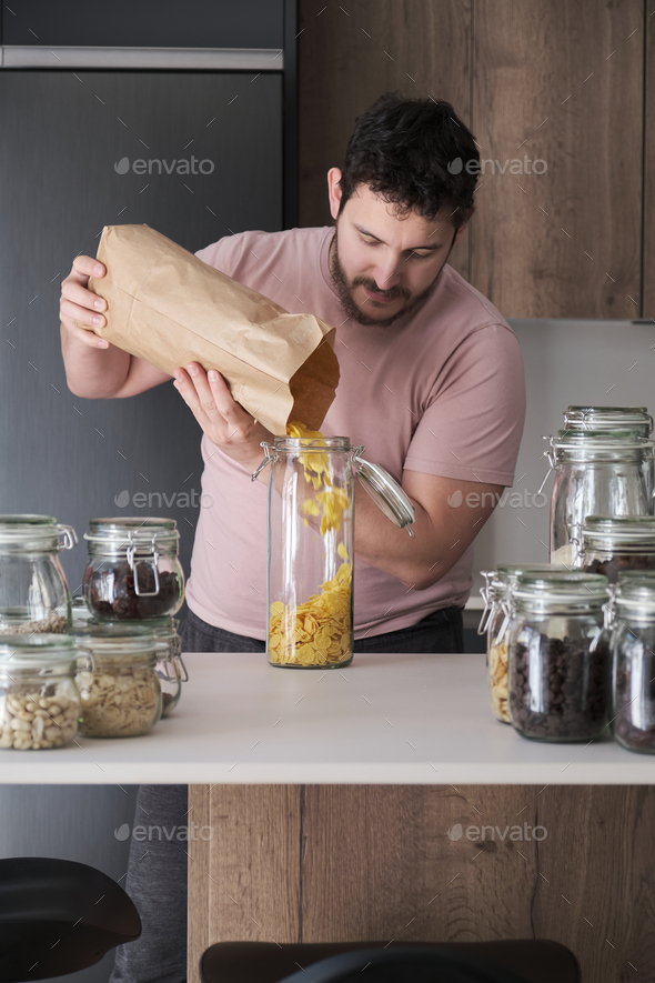 Young latin man filling up a jar with corn flakes from a paper bag.