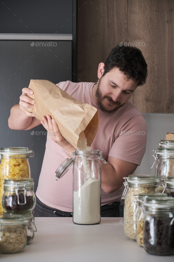 Young latin man filling up a jar with wheat flour from a paper bag.